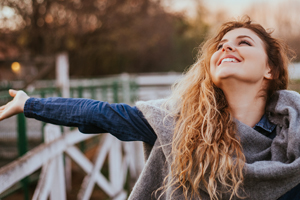Smiling young woman with open arms looking up