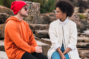 Man and woman sitting on rock shoreline talking