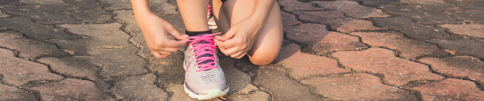 Young person tying shoelace on cobble stone path