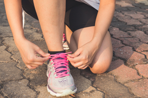 Young person tying shoelace on cobble stone path