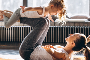 Mom on floor balancing young daughter on bent legs as in flight