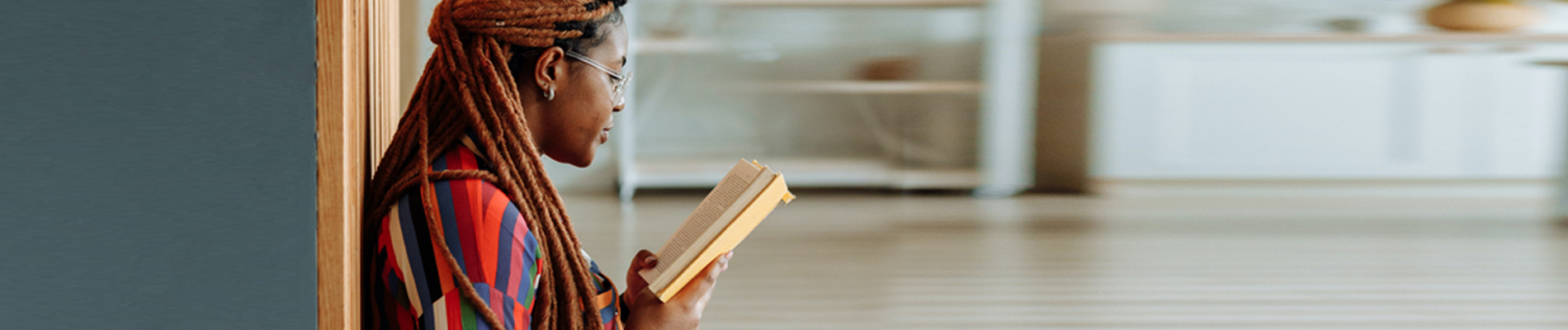 African American woman leaning against wall reading a book