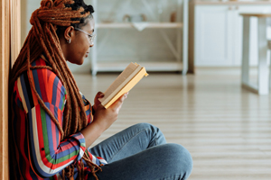 African American woman leaning against wall reading a book
