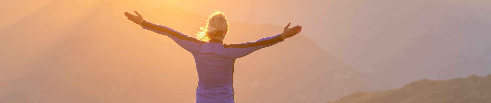 Woman with outstreached arms looking into a sunny valley