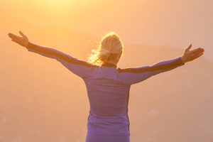 Woman with outstretched arms looking into a sunny valley