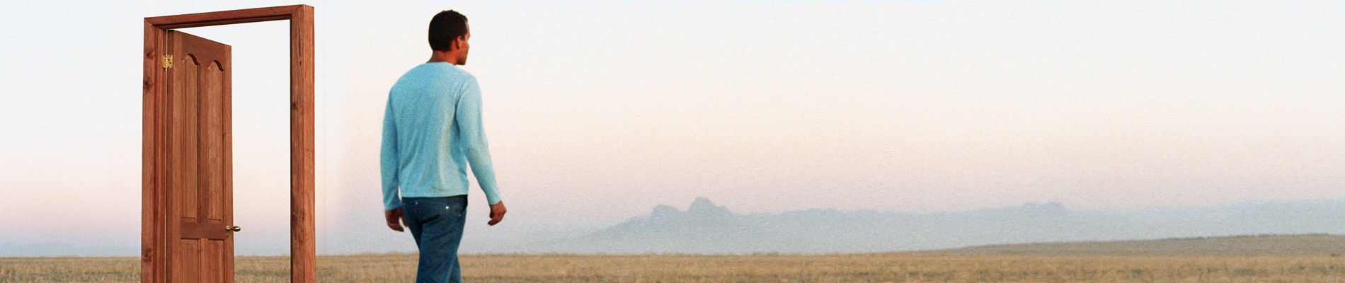 Man walking through a free-standing doorway on a grassy plateau