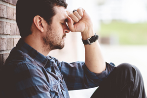 Man sitting leaning against brick pillar in contemplation