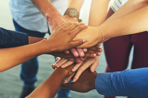 Seven hands joined/stacked in a circle indicating unity and commitment