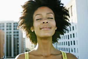 Woman smiling with eyes closed, city view behind her