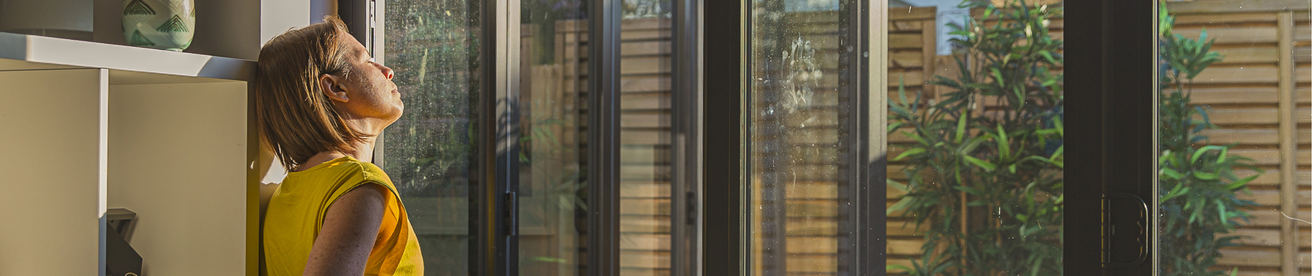 woman gazing out patio door window into the sunlight