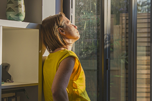 woman gazing out patio door window into the sunlight