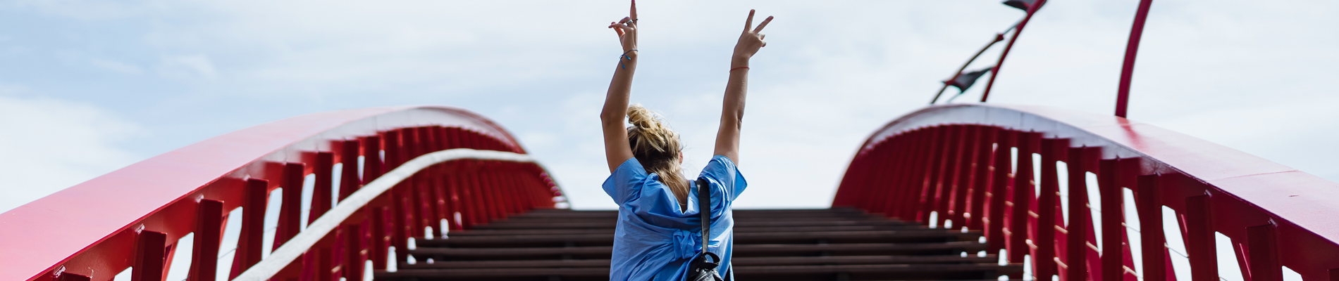 woman with arms raised in clelebration at the top of an arched walkway bridge