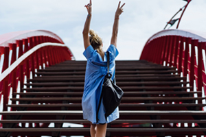 woman with arms raised in celebration at the top of an arched walkway bridge