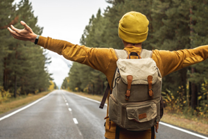 male hiker standing looking away down an empty highway through a wooded forest