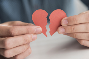 hands holding a paper heart with a tear through the middle