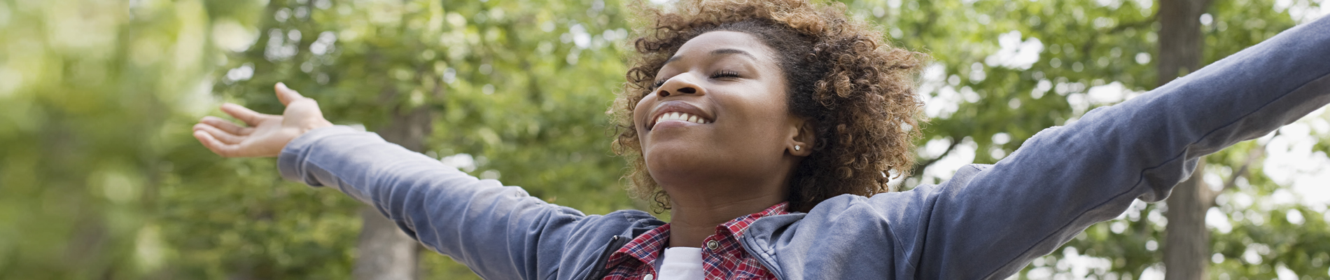 Woman in nature with head tilted back, eyes closed with out stretched arms