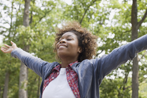 Woman in nature with head tilted back, eyes closed with out stretched arms