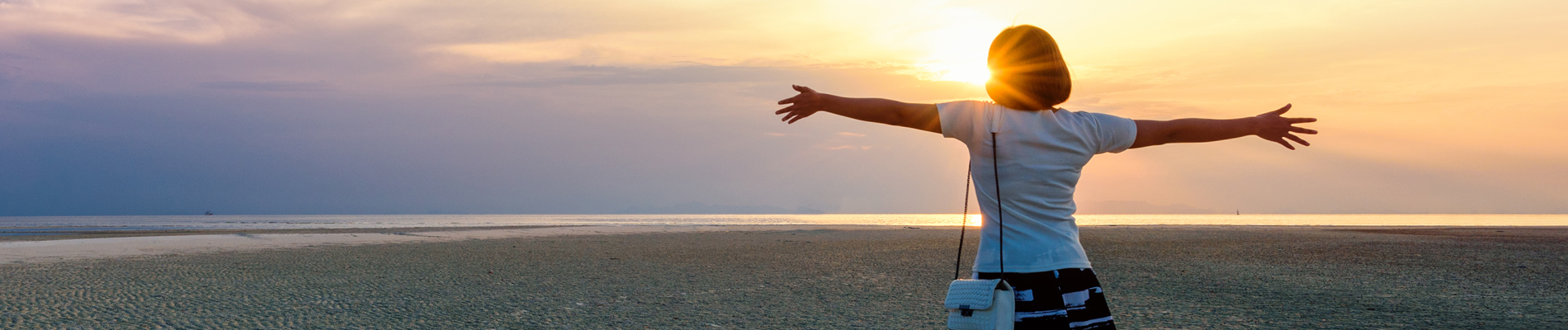 woman with outstretched arms at low tide looking towards sky