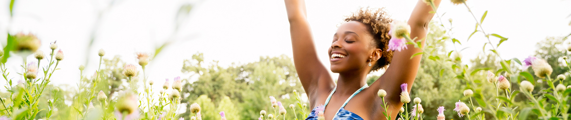 young woman arms raised walking in a tall field of blossoms