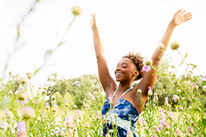 young woman arms raised walking in a tall field of blossoms
