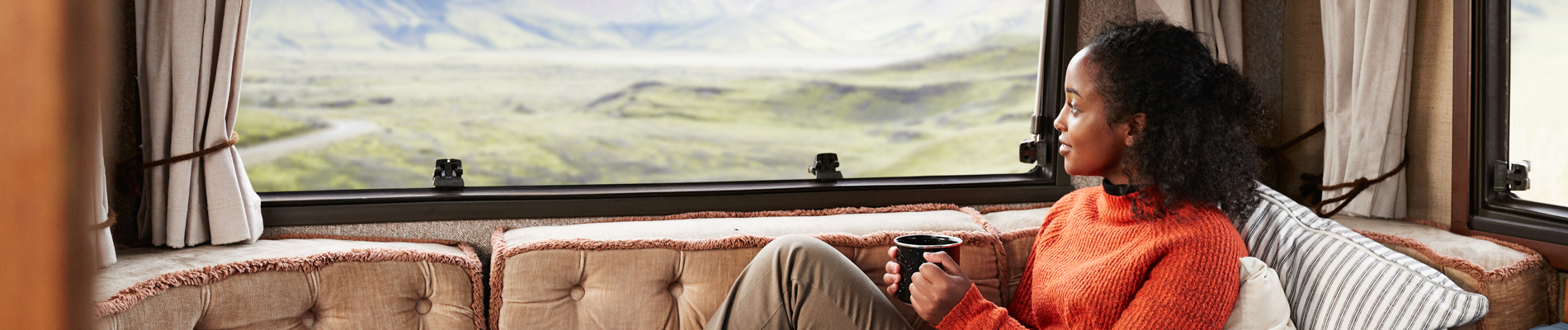 Woman sitting on a couch looking out an RV window over a valley