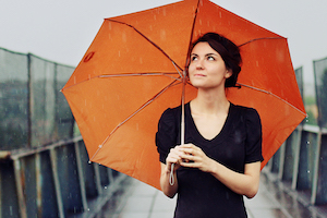 Woman walking on a metro street holding an open umbrella on shoulder