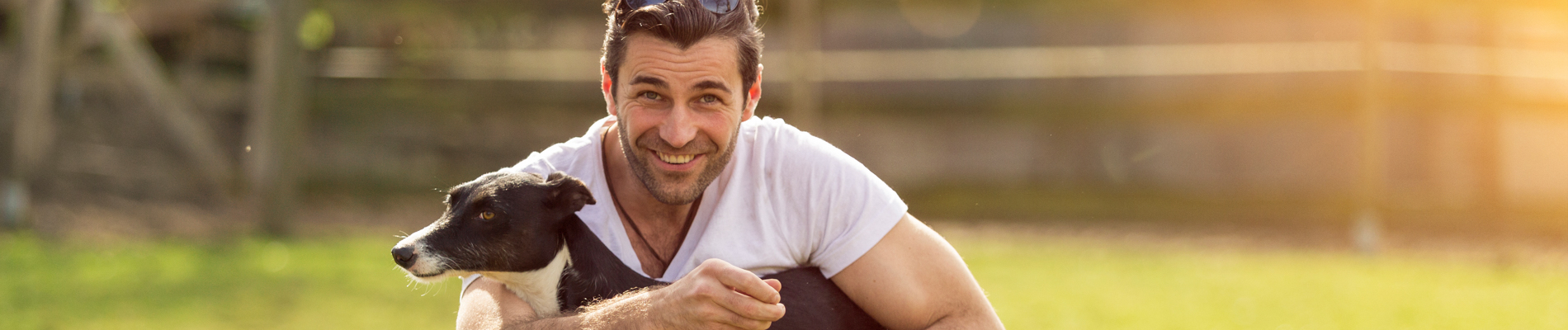 A man holding his dog on a grassy area smiling
