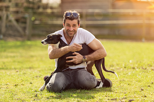 A man holding his dog on a grassy area smiling