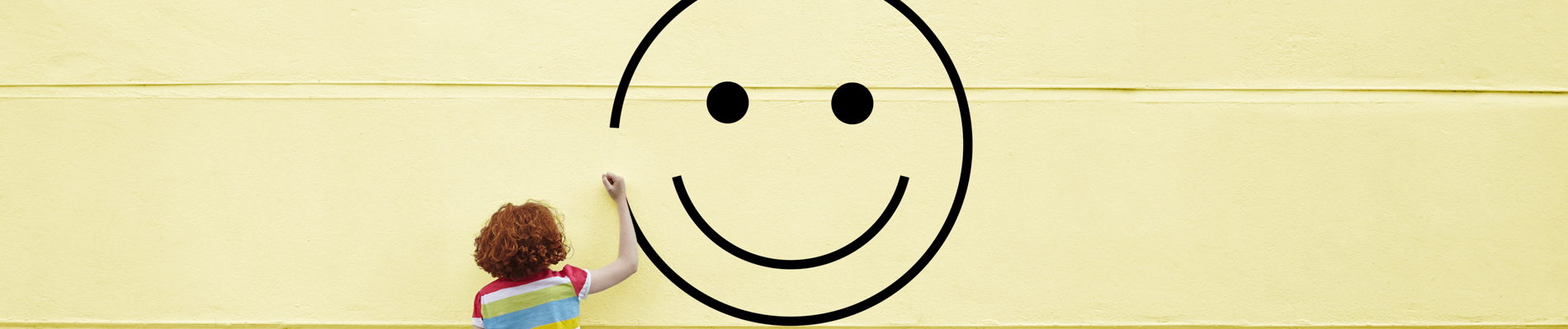 A boy drawing a smiley face on a yellow wall