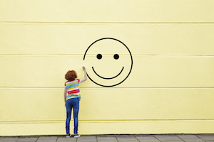 A boy drawing a smiley face on a yellow wall