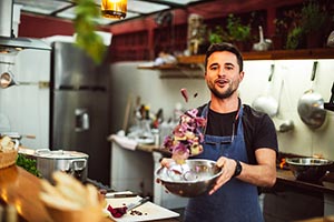 A man in a professional kitchen talking about making and tossing a salad