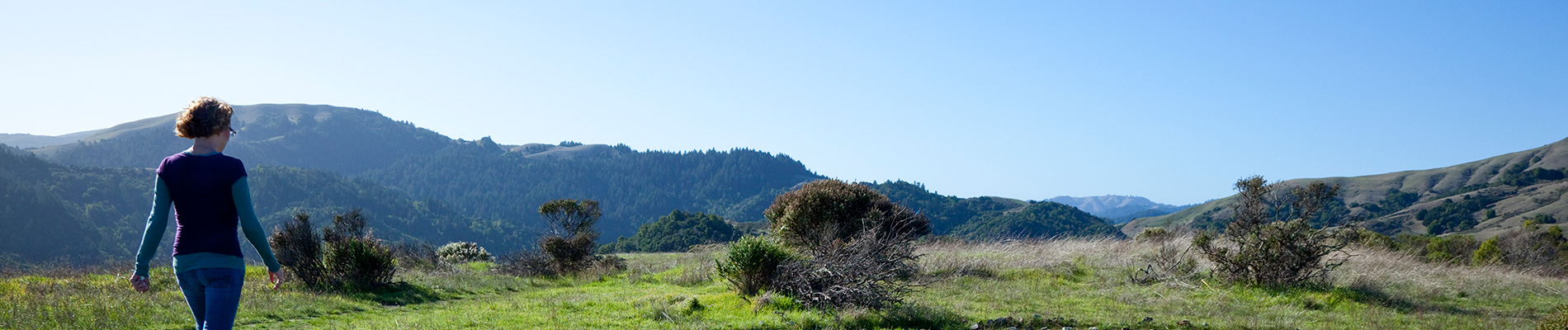 A woman walking a path through a field in a hilly area