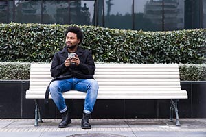 A young man standing by a hedge holding a cell phone
