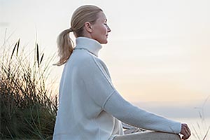 A woman in a sited yoga position near grassy dunes meditating