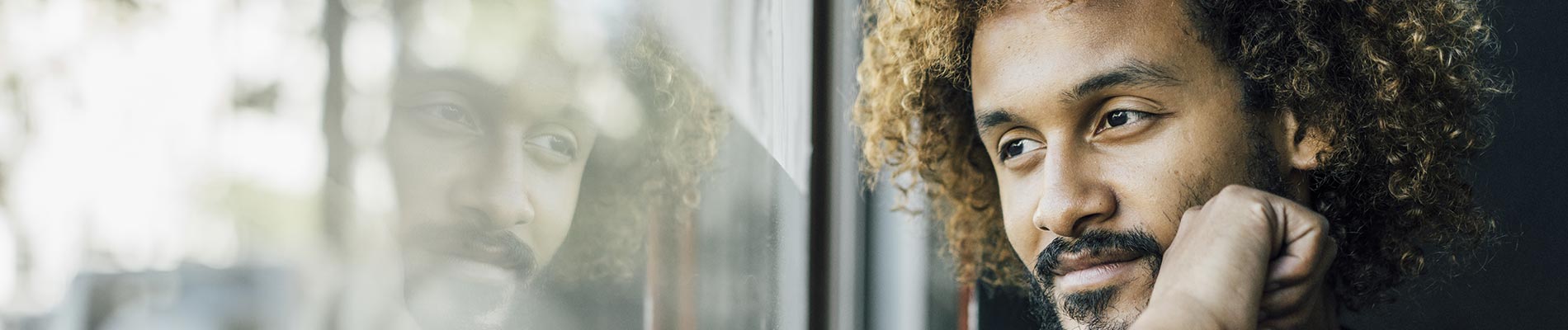 Man gazing out window seeing his reflection