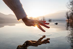 A woman's hand over water with drops fall making ripples