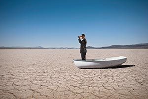 A man in a suit looking through field glasses standing in a boat on a dry lake bed