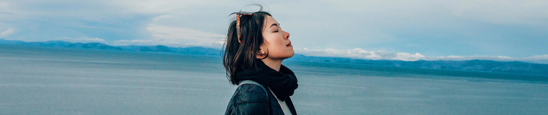 A woman with closed eyes head tilted back near a lake