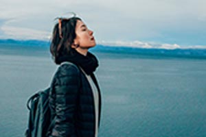 A woman with closed eyes head tilted back near a lake