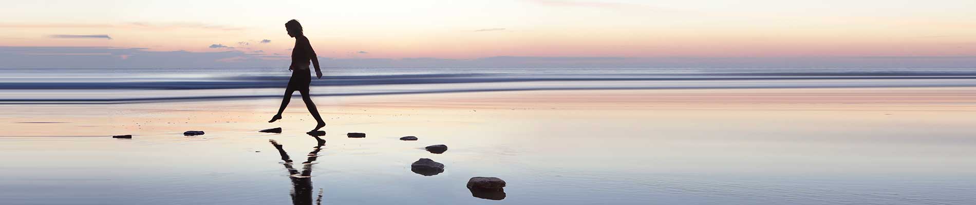 Woman walking a rock path in shallow waters along a beach