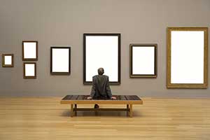 A man sitting on a bench within a room with seven blank picture frames