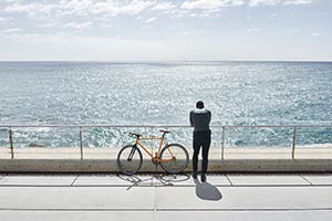 A man standing near his bike at a railing overlooking a body of water