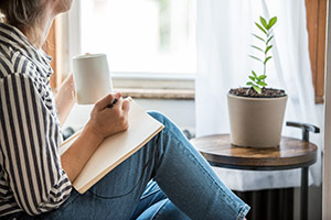 Woman sitting with a cup of coffee and a notepad on her lap