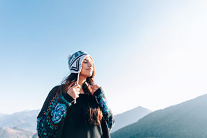 A woman in a stocking cap and wrap with mountains in the background
