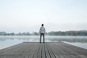 A young man standing on a dock looing over a lake with steam rising