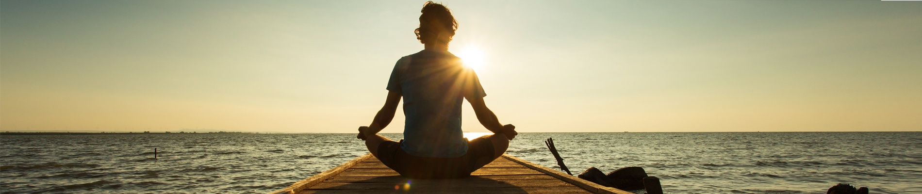 man sitting on a dock in a yoga type position facing a sun rise
