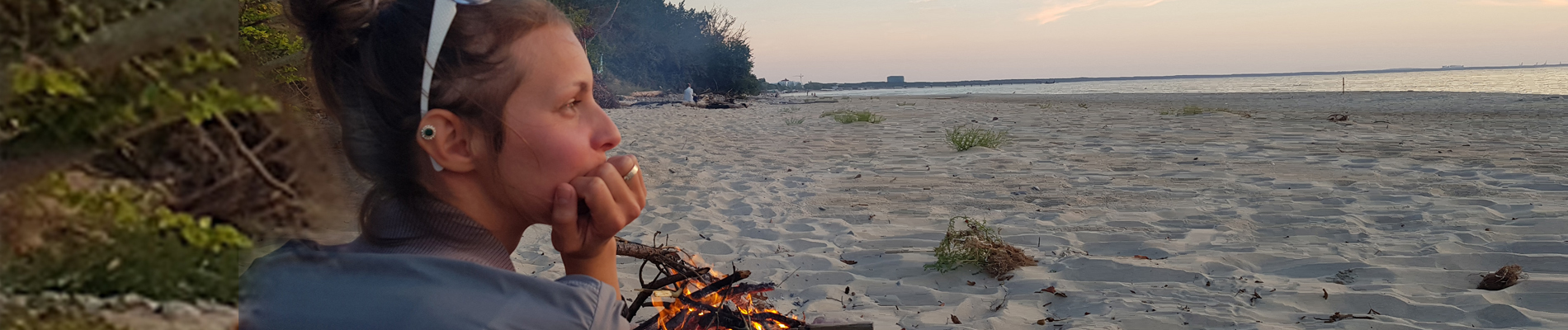 a young woman sitting by a small fire in the sand along side the ocean in thought