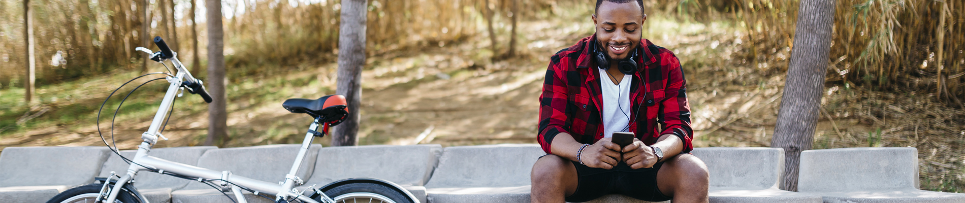 a man sitting on a park bench next to his bike texting