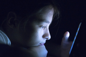 an adolescent looking at a computer screen in a dark room