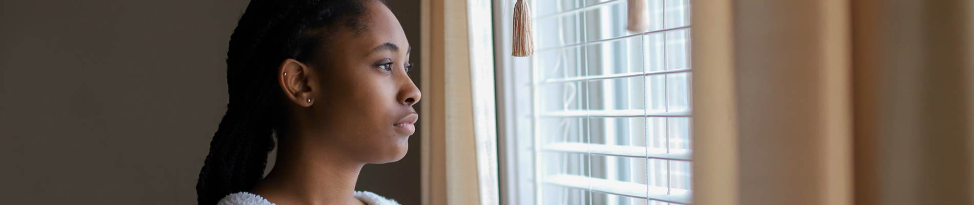 a young woman looking through the window shades to a bright outside